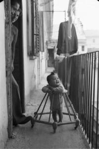 Italia Dopoguerra. Milano - Quartiere cinese - bambino cinese si muove con il girello sul ballatoio di una casa a ringhiera sotto lo sguardo attento di una coppia di persone