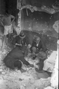 Italia Dopoguerra. Milano - Gruppo di uomini gioca a carte tra le macerie mentre un bambino in piedi li osserva