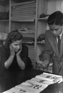 Italia Dopoguerra. Milano - Quartiere cinese - un uomo cinese traccia ideogrammi su un foglio mentre una donna lo osserva