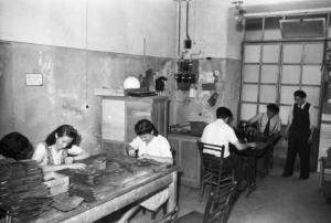 Italia Dopoguerra. Milano - Quartiere cinese - coppia di donne lavora la pelle - Sullo sfondo alcuni uomini cinesi lavorano con la macchina da cucire