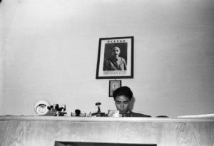Italia Dopoguerra. Milano - Quartiere cinese - un uomo cinese siede con espressione seria alla sua scrivania - Alle sue spalle un ritratto appeso alla parete
