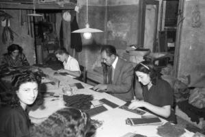 Italia Dopoguerra. Milano - Quartiere cinese - operai al lavoro intorno a un tavolo realizzano portafogli in pelle