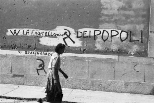 Italia Dopoguerra. Trieste - Donna cammina rasente a un muro riportante le scritte "W LA FRATELLANZA DEI POPOLI"  e "W STALINGRADO" con il simbolo della falce e martello