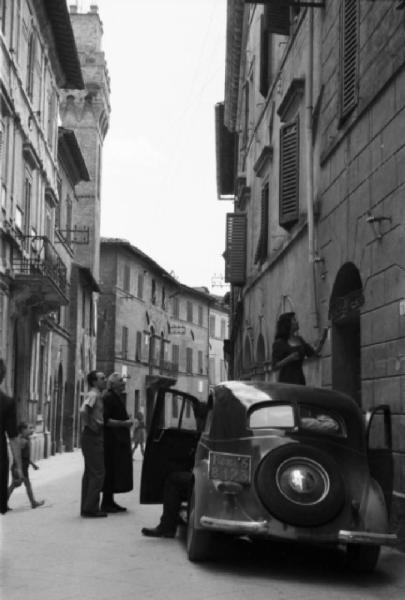 Italia Dopoguerra. Buonconvento - automobile parcheggiata lungo una via - Lina Bo