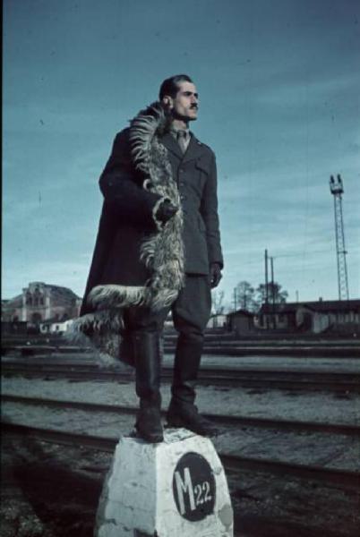 Campagna di Russia. Ritratto maschile - Militare italiano indossa pelliccia di montone e posa in piedi su una pietra migliare tra i binari ferroviari