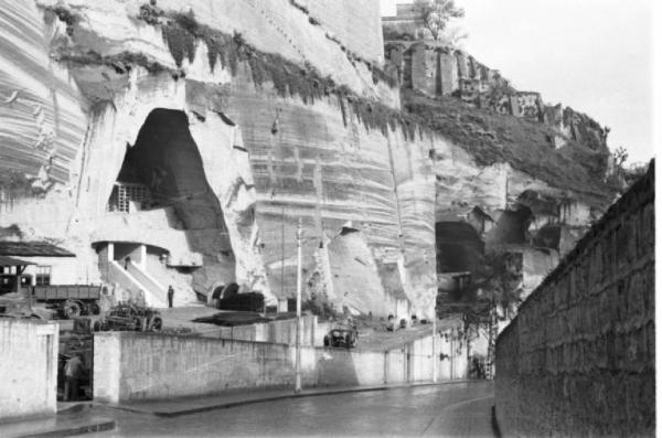 Italia Dopoguerra. Napoli. Strada corre a fianco di una scarpata in tufo con edificio scavato all'interno