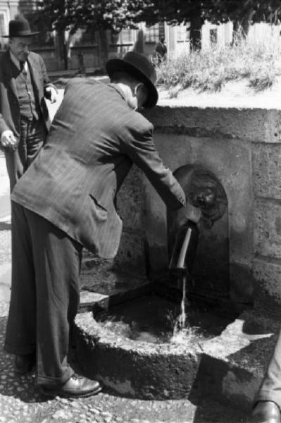 Milano. Parco Sempione. Un uomo riempie una bottiglia d'acqua alla "Fontana dell'acqua marcia" - un altro uomo osserva