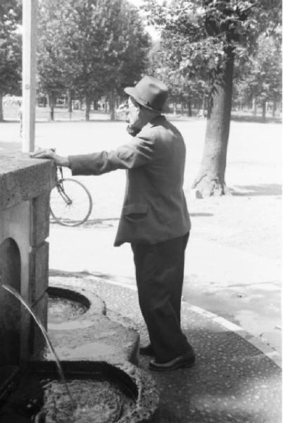 Milano. Parco Sempione. Uomo che beve da un bicchiere riempito alla "Fontana dell'acqua marcia"