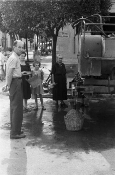 Una famiglia con secchio e fiasco attende di riempirli con l'acqua delle cisterne collocate per strada