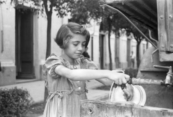 Una bambina alle prese con il rubinetto di una cisterna dell'acqua collocata per la strada