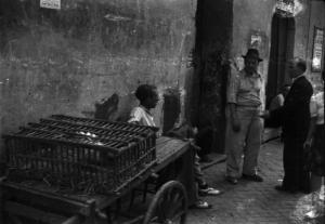 Italia Dopoguerra. Roma - Quartiere Trastevere - Ambulante accanto al proprio carretto che trasporta una stia di polli