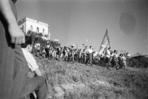 Invasione delle terre. Gruppo di contadini che manifestano scendendo lungo un prato con una bandiera alla testa del corteo