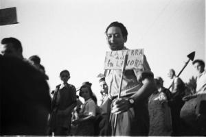 Invasione delle terre. Gruppo di contadini che manifestano. Un uomo tiene in mano un cartello con scritto "la terra a chi la lavora":