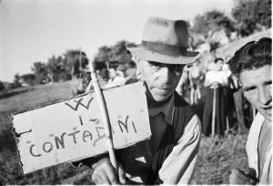 Invasione delle terre. Gruppo di contadini che manifestano in un prato. Primo piano di due uomini con in mano un cartello con la scritta "W i contadini"