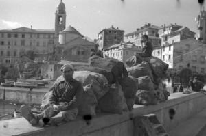 Italia Dopoguerra. Nervi - Scorcio del porto - In primo piano un uomo siede su un parapetto appoggiandosi ad alcuni sacchi