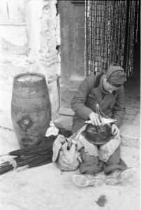 Italia Dopoguerra. Terracina. Un militare seduto sulla soglia di un'abitazione leviga il fondo di una pentola