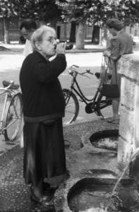 Milano. Parco Sempione. Una donna anziana beve da una fiaschetta riempita alla "Fontana dell'acqua marcia"