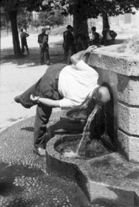 Milano. Parco Sempione. Uomo che si disseta alla "Fontana dell'acqua marcia" - sullo sfondo un gruppo di persone che discute
