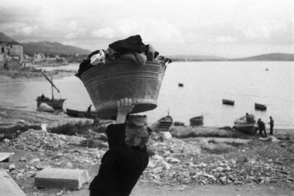 Italia Dopoguerra. Formia. Una donna anziana con un cesto di biancheria si reca verso il mare
