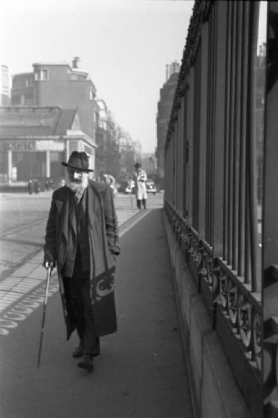 Parigi. Un uomo anziano con bastone cammina per la strada a fianco di una cancellata