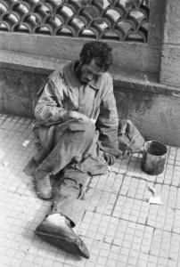Italia Dopoguerra. Napoli. Un uomo con una fasciatura ad un piede chiede la carità seduto accanto a un muro