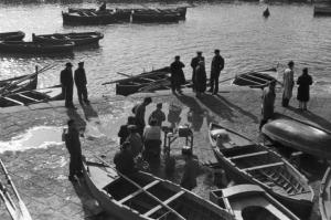 Italia Dopoguerra. Pozzuoli. Gruppo di persone presso il porto, piccole imbarcazioni in secca e una donna vende cibi pronti