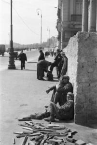 Italia Dopoguerra. Napoli. Veduta di via Caracciolo: due persone sedute per terra e un lustrascarpe. Automezzi lungo la strada