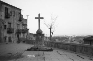 Italia Dopoguerra. Scorcio di un paese, una piazza con monumento con crocefisso
