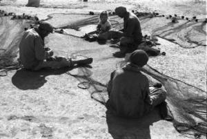 Italia Dopoguerra. Mondello. I pescatori sistemano le reti, con loro siede per terra una bambina