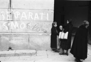 Italia Dopoguerra. Palermo. Donne anziane parlano all'angolo di una strada. Muro con scritta "SEPARATISMO"