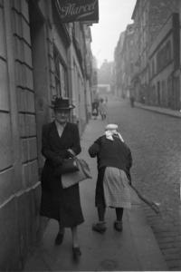 Parigi. Il quartiere di Montmartre. Due donne anziane: una vestita elegantemente cammina lungo la strada, l'altra spazza il marciapiede