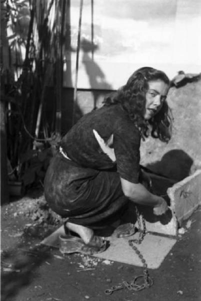 Italia Dopoguerra. Milano - Periferia - Baraccopoli - Ritratto femminile, ragazza attinge l'acqua dal pozzo