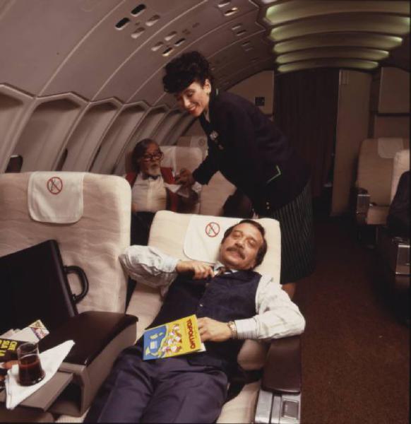 Campagna pubblicitaria Alitalia. Interno di aeromobile - business class - uomo riposa - hostess serve una bibita