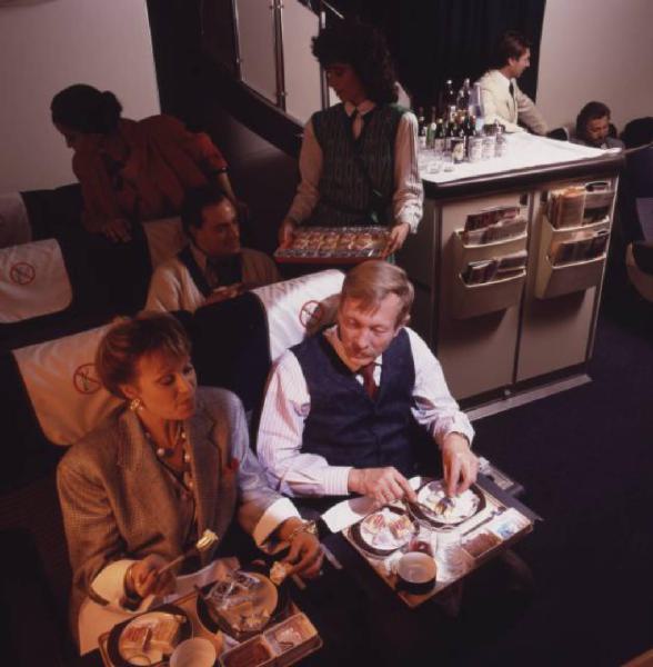 Alitalia. Interno della business class di un aeromobile - passeggeri e hostess durante il servizio pranzo