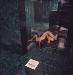 Ceramiche artistiche Piemme. Nudo femminile posa all'interno di un bagno chiusa in una scatola di plexiglass - in primo piano una piastrella con il marchio dell'azienda