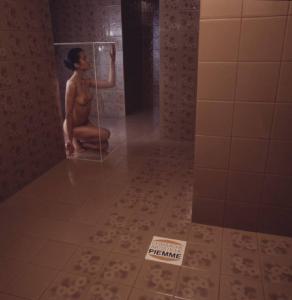 Ceramiche artistiche Piemme. Nudo femminile posa all'interno di un bagno chiusa in una scatola di plexiglass - in primo piano una piastrella con il marchio dell'azienda