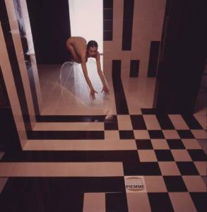 Ceramiche artistiche Piemme. donna posa sopra un cuneo di plexiglass all'interno di un bagno - in primo piano una piastrella con il marchio dell'azienda
