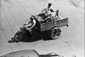 Italia Dopoguerra. Roma. Via Veneto. Mototaxi a tre ruote con cassone posteriore che trasporta una coppia con valige