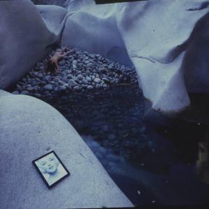 Val Verzasca - coppia di fotomodelle in vestaglia bianca immobili in piedi all'interno di una conca ghiaiosa. In primo piano una riproduzione del volto di Marilyn Monroe