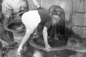 Milano. Parco Sempione. Una donna anziana si rinfresca bagnandosi il capo alla "Fontana dell'acqua marcia"