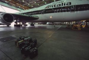 Alitalia. Interno di un hangar - aeroplano bireattore della compagnia di bandiera e valigie appoggiate sul pavimento