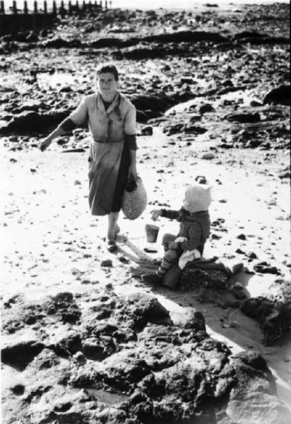 Cascais. Spiaggia con la bassa marea - donna alla ricerca di molluschi. Accanto bambino seduto su uno scoglio