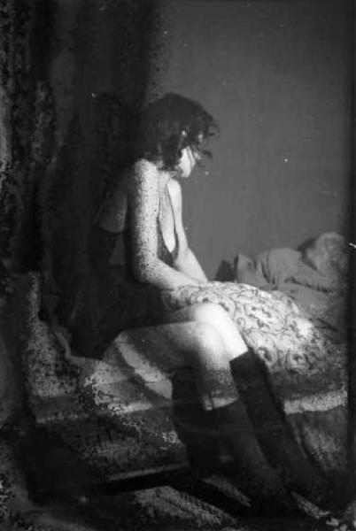 Una prostituta seduta sul letto con biancheria intima e stivali