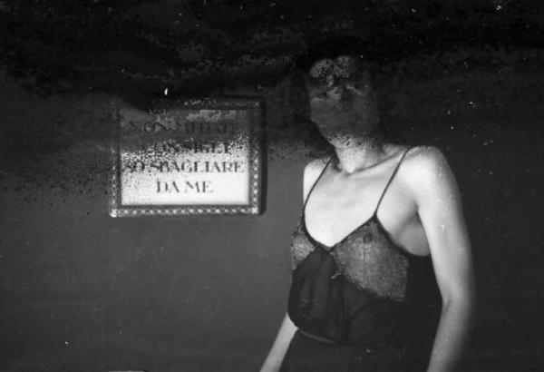 Una prostituta in una stanza - sul muro il cartello "NON MI DATE CONSIGLI - SO SBAGLIARE DA ME"