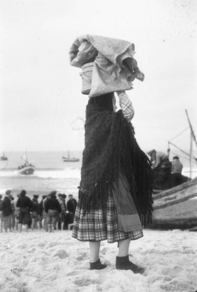 Spiaggia di Nazaré - donna osserva il rientro dalla pesca trasportando masserizie sul capo