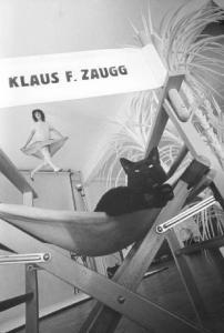 Set fotografico - modella sospesa nel vuoto - sedia da regista con scritta "Klaus Zaugg" - gatto nero