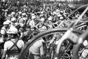 Giro d'Italia. Ciclisti in piazza. In primo piano il particolare di una ruota e un manubrio