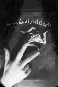 Stoffa con la scritta "LA SICILIA AI SICILIANI" e il simbolo della Trinacria - in primo piano una mano fa il segno delle tre dita