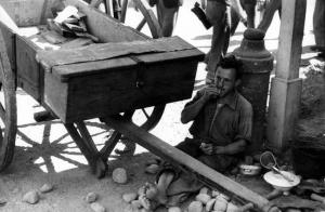 Italia Dopoguerra. Milano - Un uomo consuma il proprio pasto seduto a terra accanto a un carro