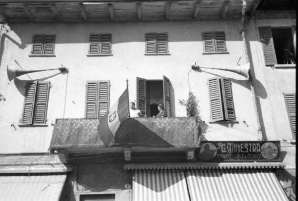 Italia Dopoguerra. Sant'Angelo Lodigiano. Reportage sulla figura di Santa Francesca Cabrini - scorcio dalla strada di un balcone con un gruppo bandiere monarchiche